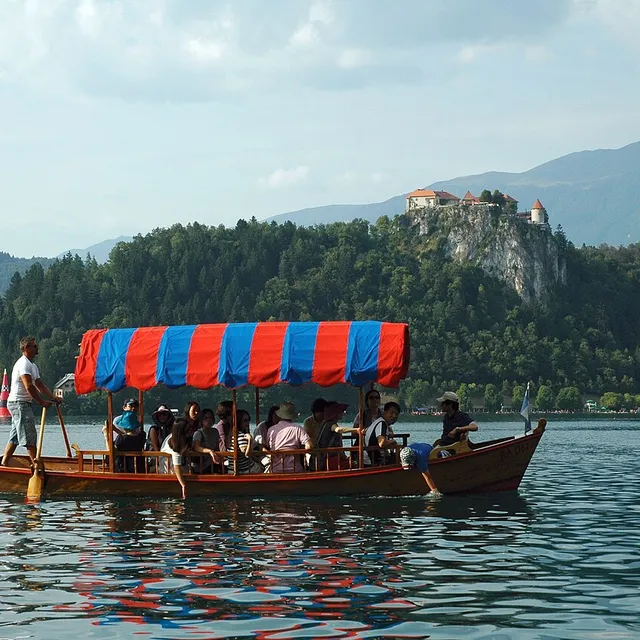 A full pletna boat crossing Lake Bled beneath the castle cliff